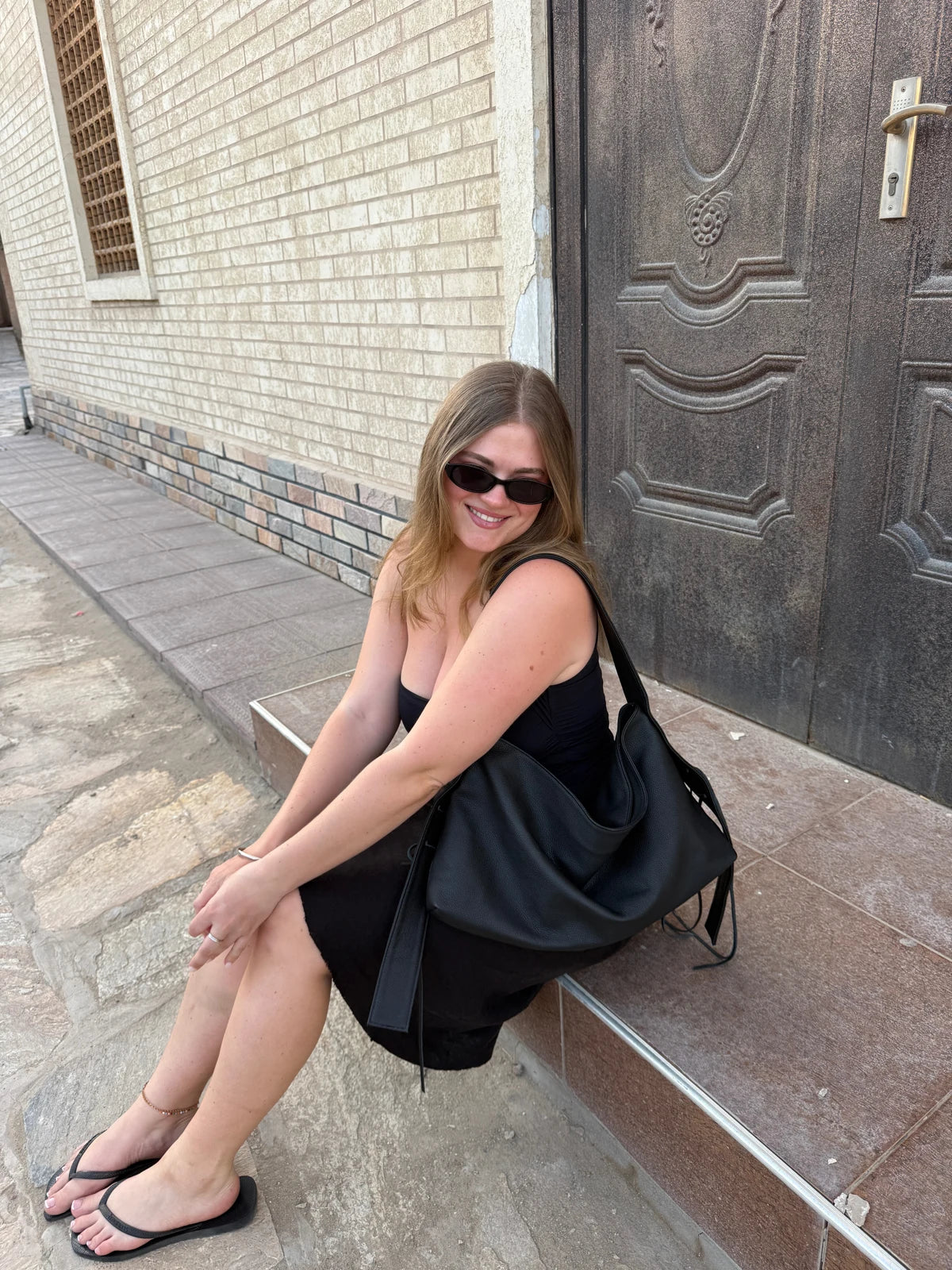 Woman wearing a black Lola Slouch bag while seated outdoors